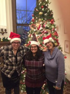 3 women in Santa hats in front of a Christmas tree.